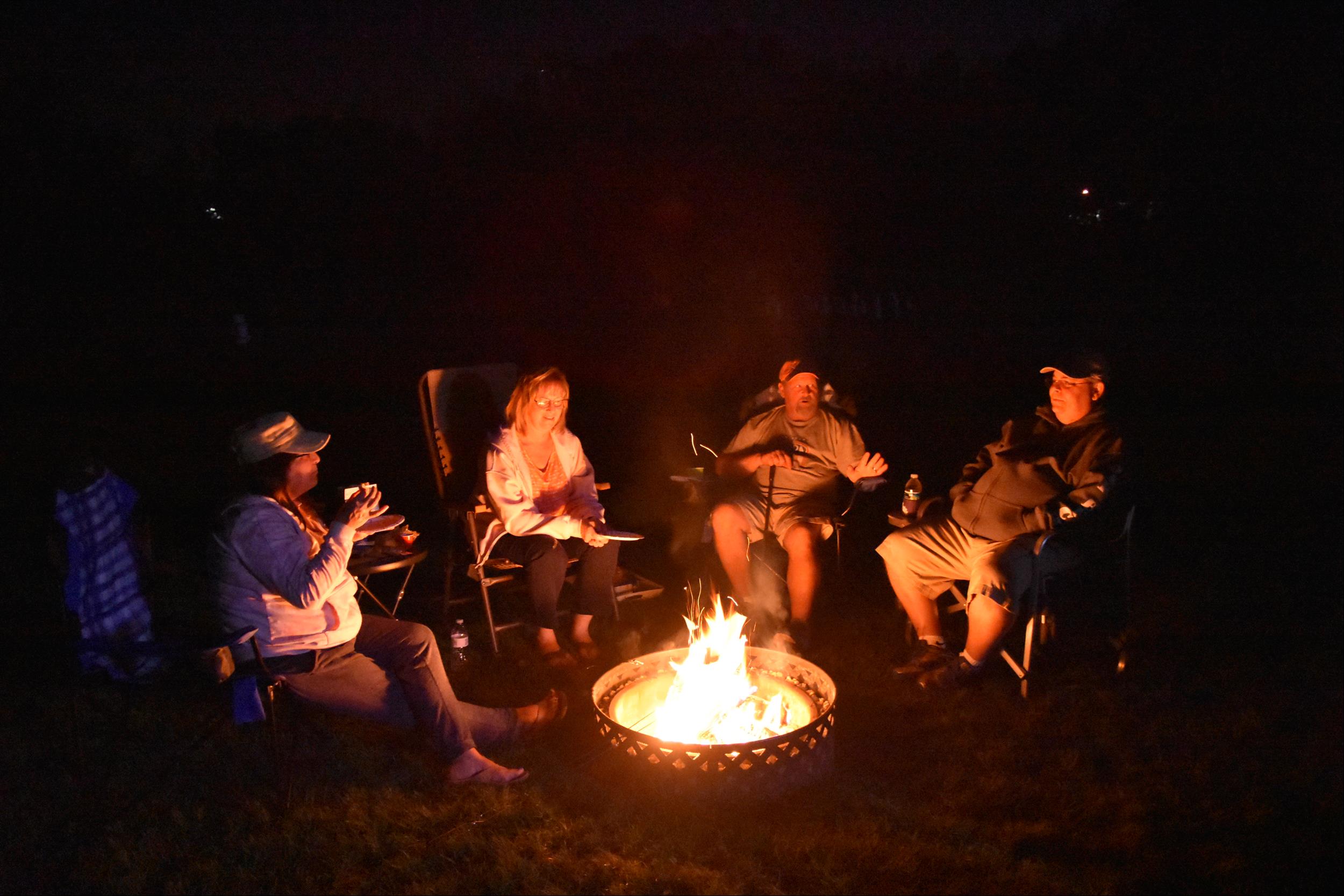 four adults sitting around campfire